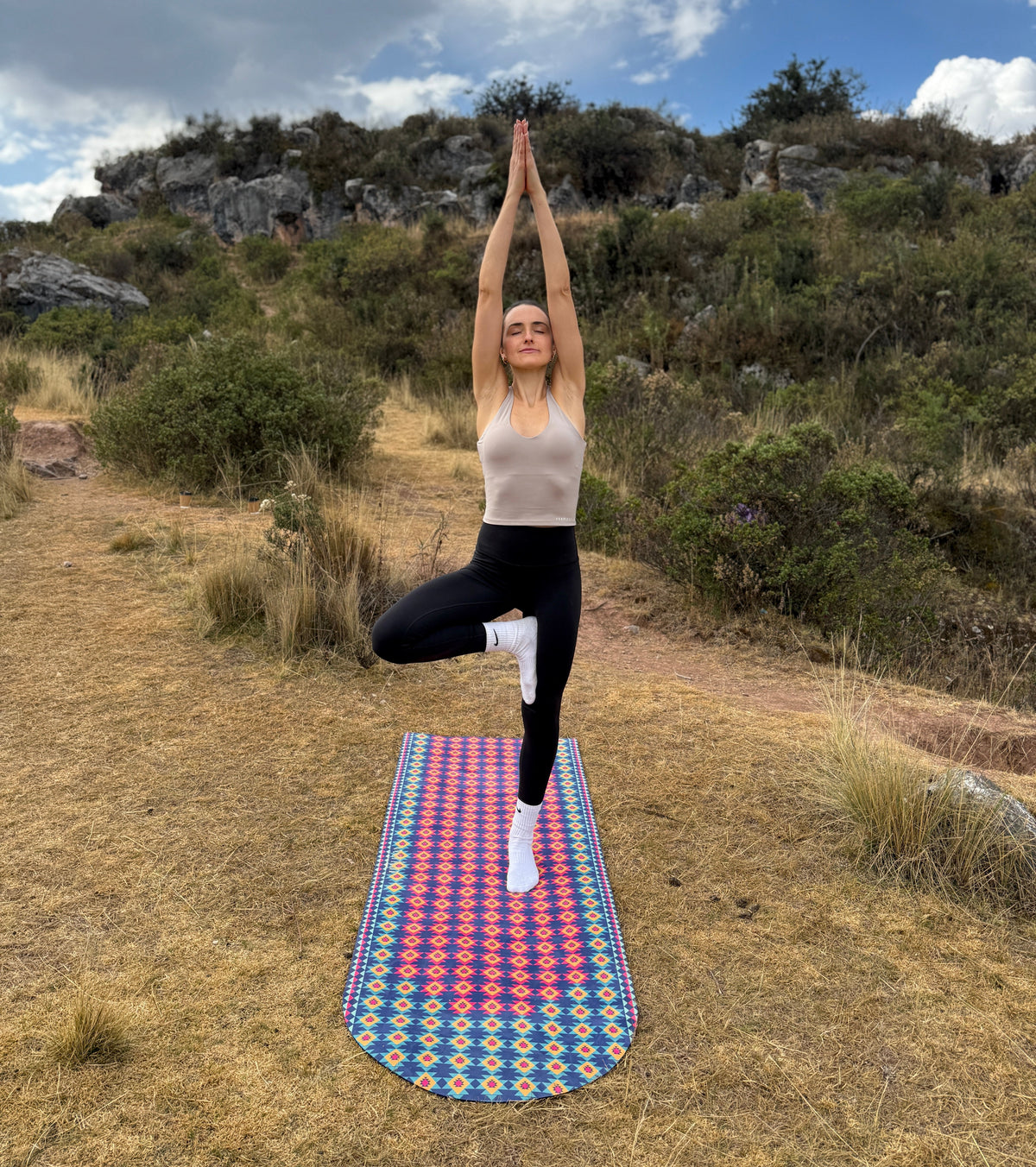 Person practicing yoga on a colorful mat outdoors with a natural landscape in the background